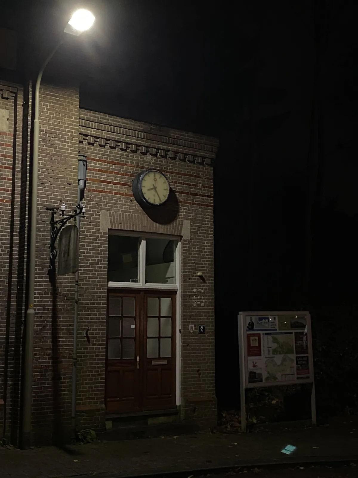 It’s dark outside. A street light shines its light on a brick building with a modernist clock on it, the classic Dutch railway kind. The clock points at 25 minutes past 8.
