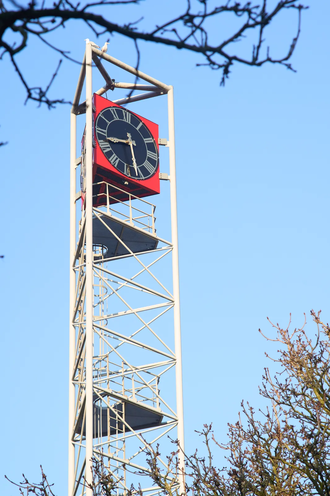 On top of a modern, white, high structure there’s a red, black golden clock. It points at 27 minutes past eight.