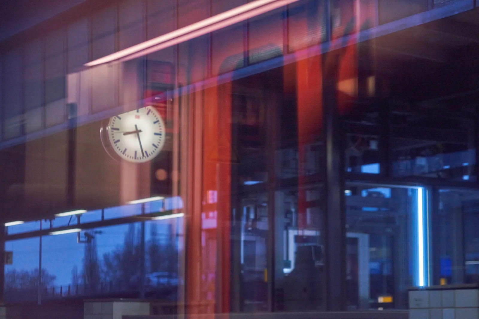 A picture taken from within a train, some interior stuff can be seen in the reflection. Outside is a clock that points at 27 past 8. 