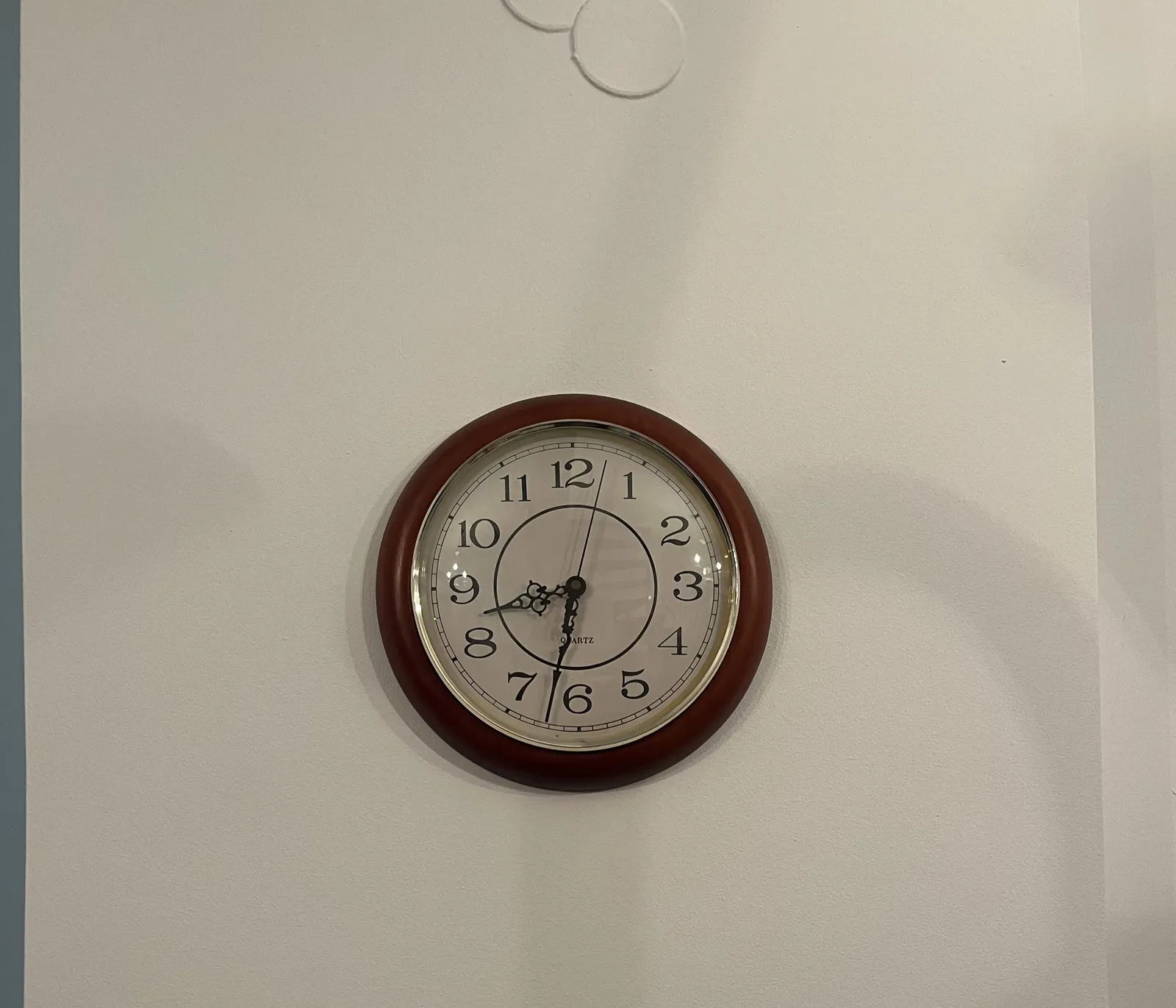 A wall clock on a white wall. There are two white plastic circles, probably covering some holes in the wall. The clock points at 32 minutes past eight.