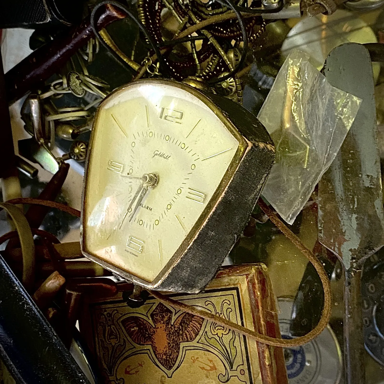 A old alarm clock laying among some other stuff. It points at eight 33.