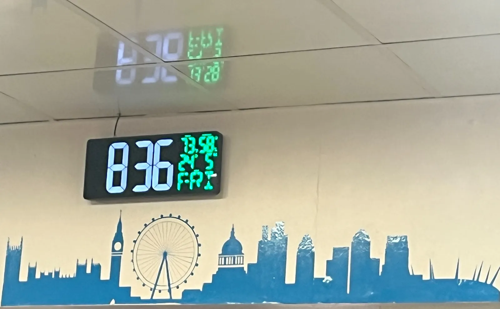 A graphical representation of the skyline of what looks like London on a wall, with a digital clock above it. There’s all kinds of info on this clock. The time is shown in very large digits as 8:36.
