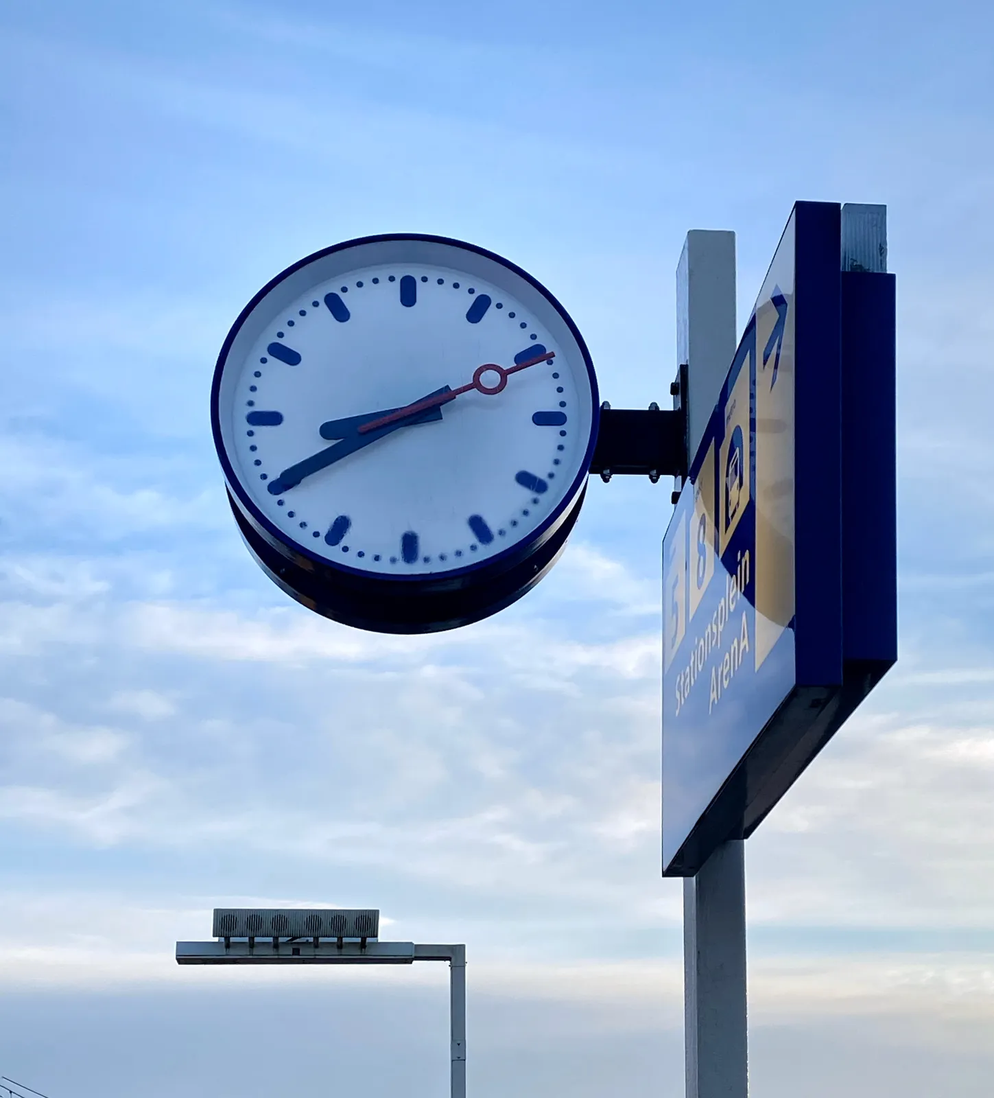 A clock in the open air, at a station in The Netherlands. It points at 20 minutes to 9.