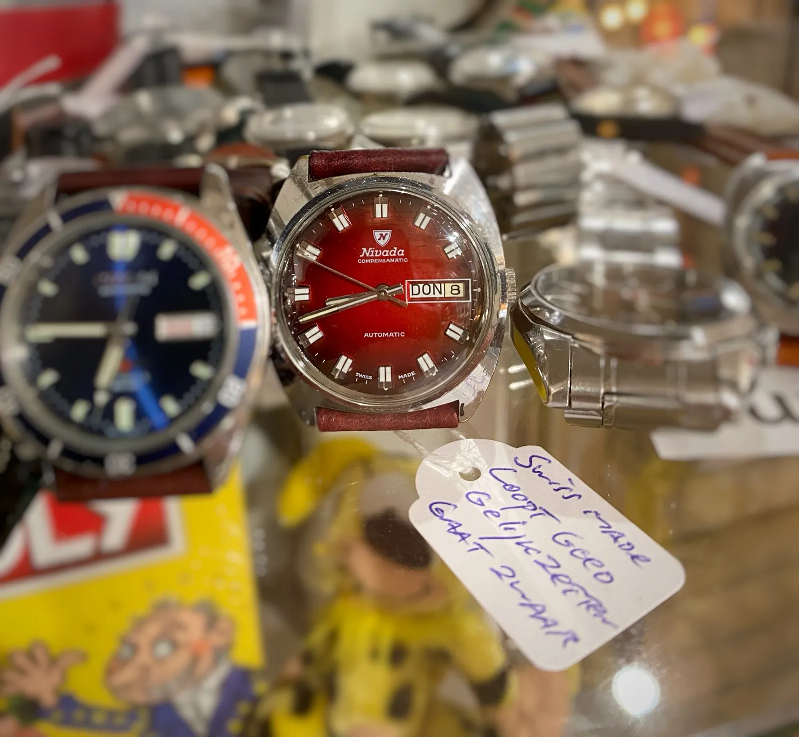 Watches on a glass plate. Only one of them, with a red face, is in focus. It points at 18 minutes to 8.
