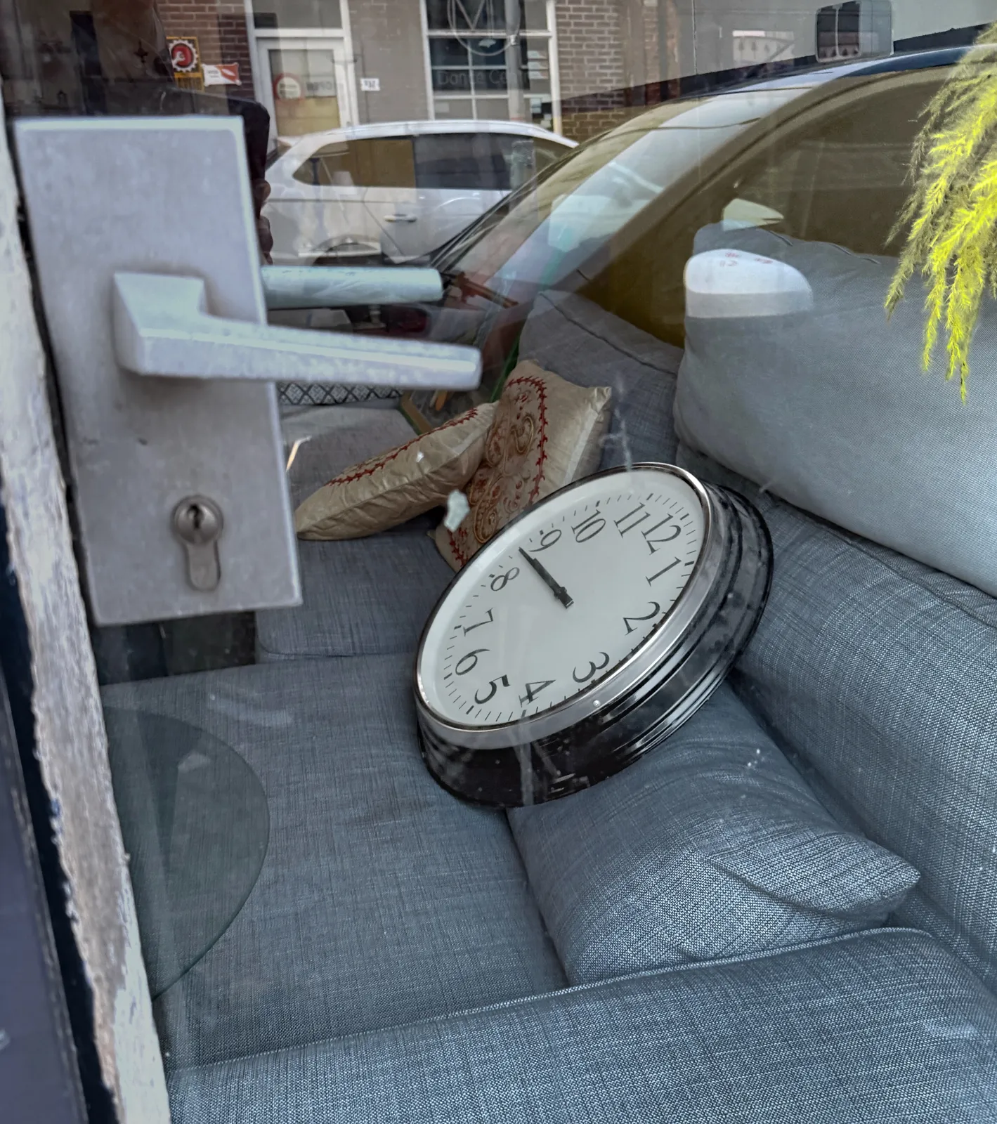 A large wall clock lays on a blue couch. It points at 17 minutes to nine.