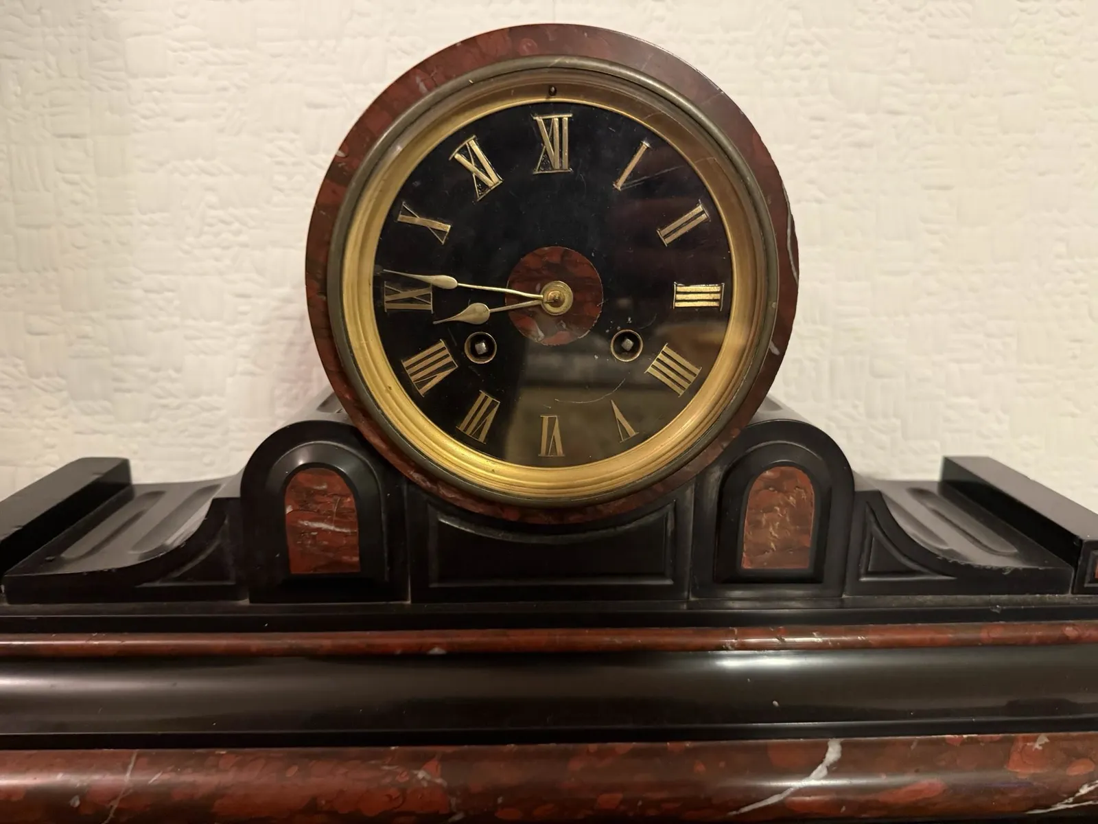 An old mantel clock. It’s made from black and red stone. It points at 14 minutes to 9.