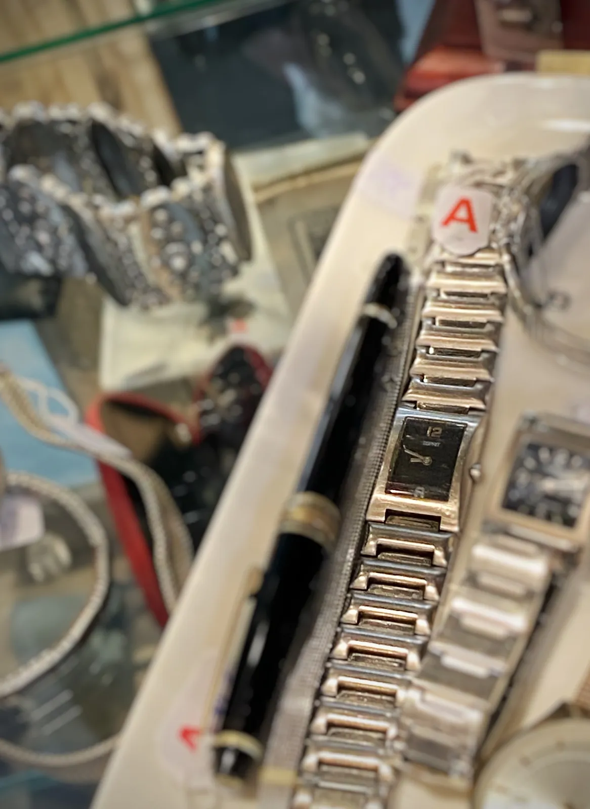 A pen and two watches for sale. One of the watches is in focus and is points at 13 minutes to 9.