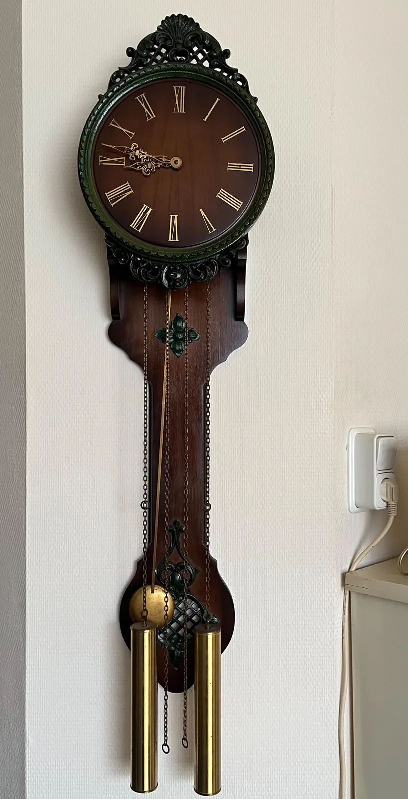 An old, dark wooden wall clock, subtly ornamented, with a long pendulum, and some heavy weights, both at exactly the same height.  It points at 13 minutes to 9