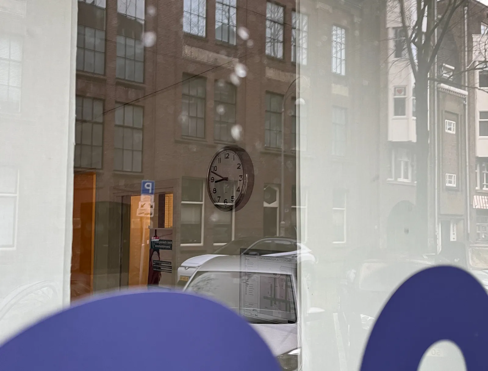 Peeking through a window. In the reflection some cars, some Amsterdam houses. In the room there’s a clock which points at 12 to nine.