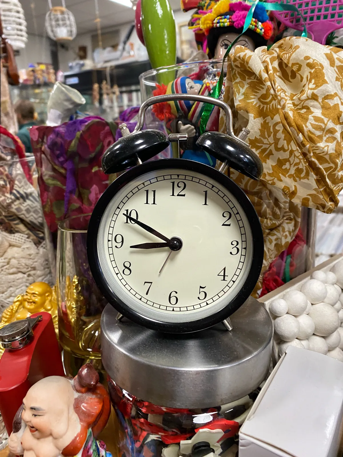 An old fashioned, black alarm clock, surrounded by colourful stuff. It points at 11 minutes to 9.