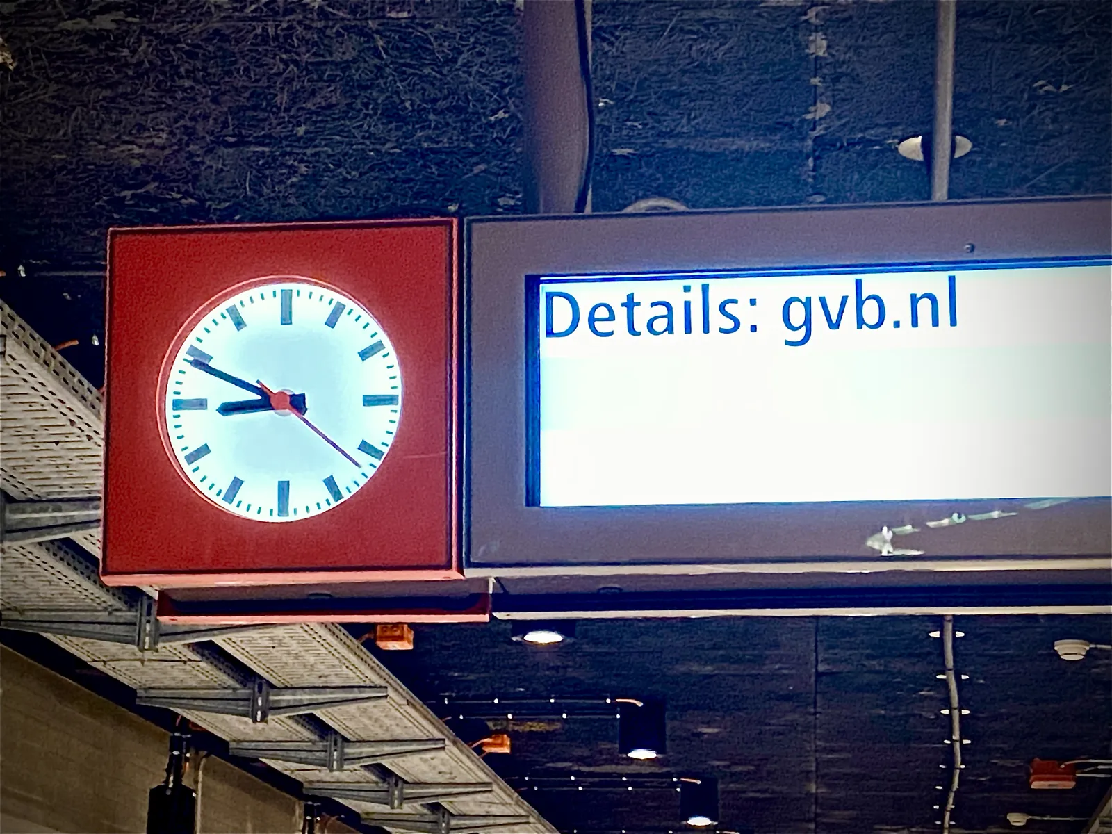 A clock in what seems to be a metro station. Next to it there’s a display that says Details gvb.nl. On the clock it is 11 minutes to 9.
