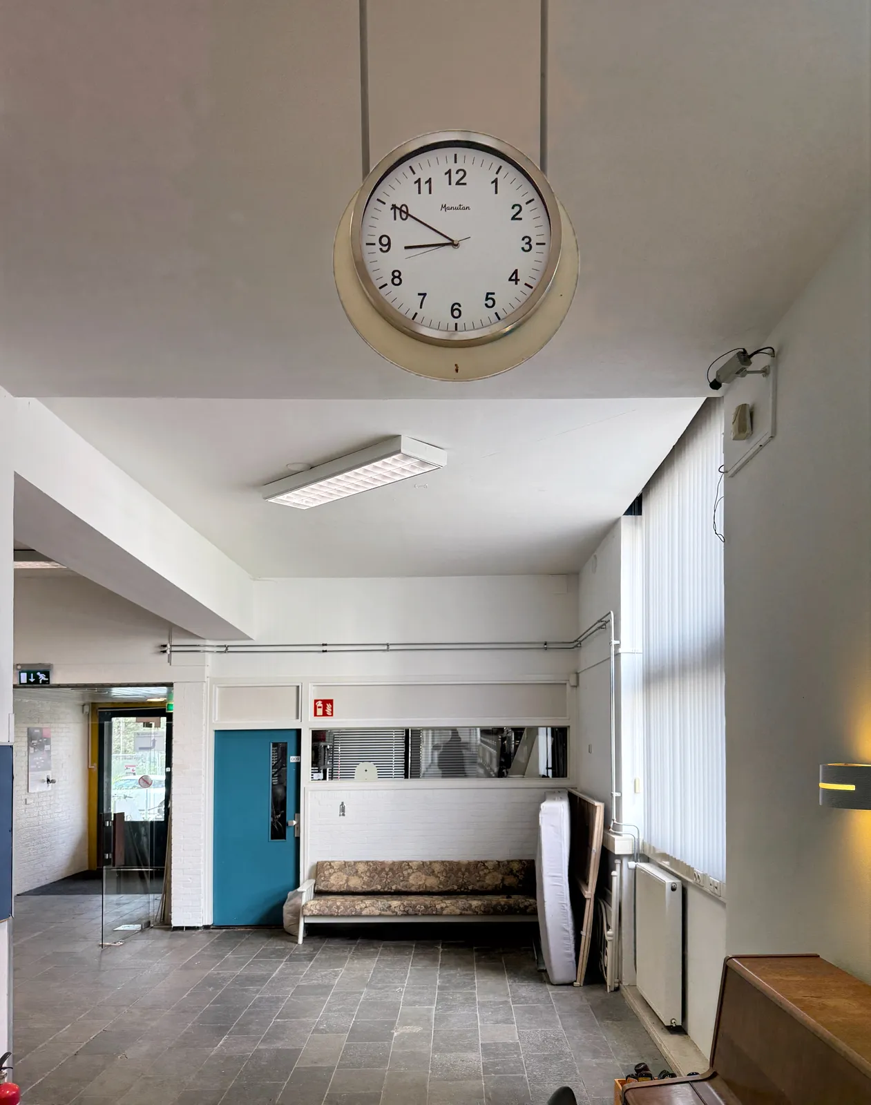 A clock hangs from a ceiling in a deserted office building. It points at 10 minutes to nine.