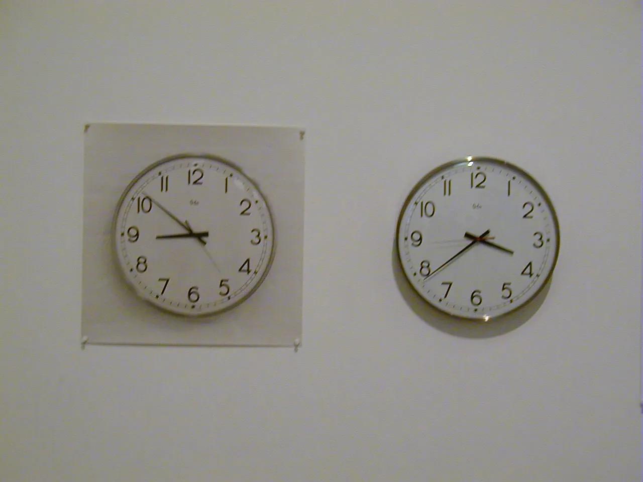 There’s a clock on the right, and left of it is a poster of the same clock, in the same size. The time on the poster is nine minutes to nine, which it is now. The real clock points at 38 past three, which it isn’t.