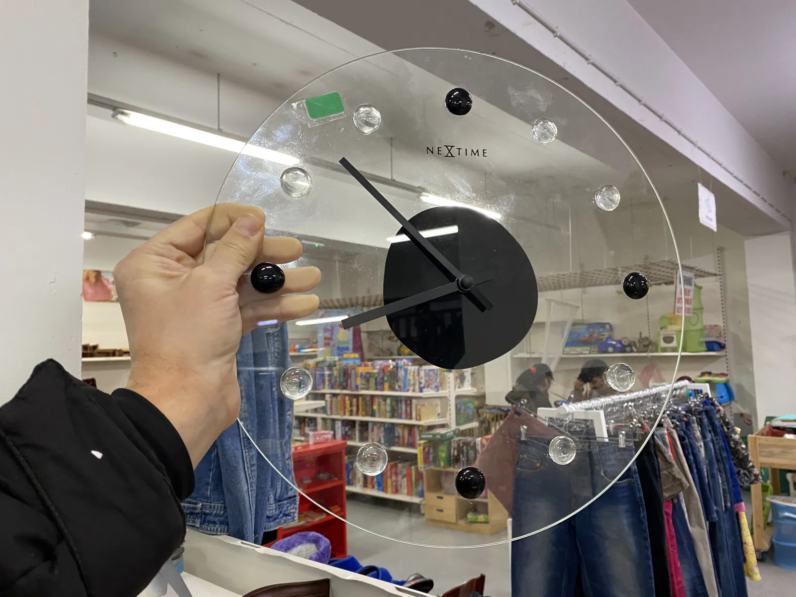 A plastic, or glass clock points at 8 minutes to nine. You can see a thrift shop through it.