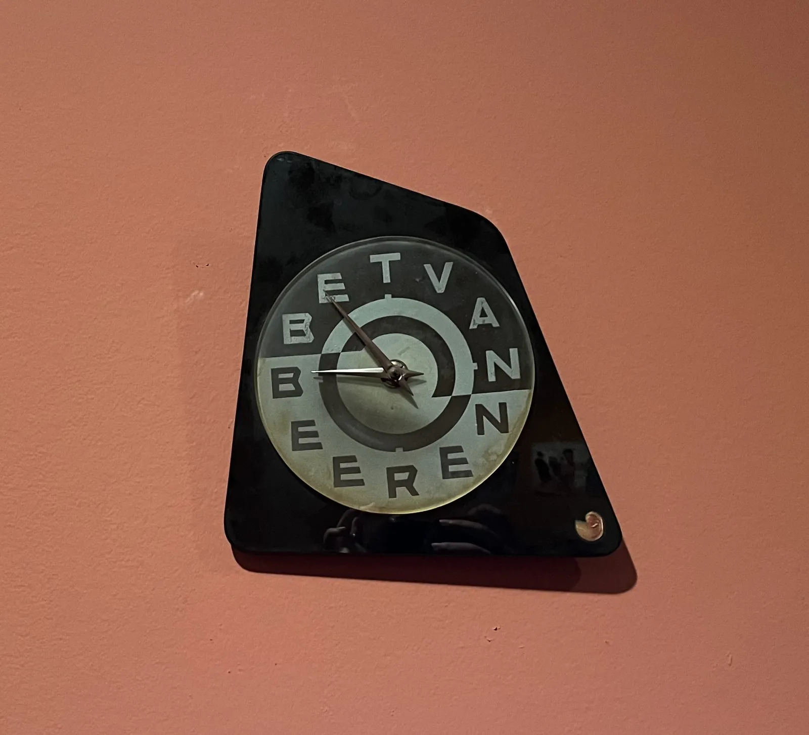A designed clock. Its outer shape is a black irregular quadrilateral. There’s a circle within this trapezium. In the cirle the name Bert van Beeren is written in large capitals, filling the complete face to the clock. The words Bert and Van are written in white on black, the word Beeren is written in black on white. The clock points at 6 minutes to 9.