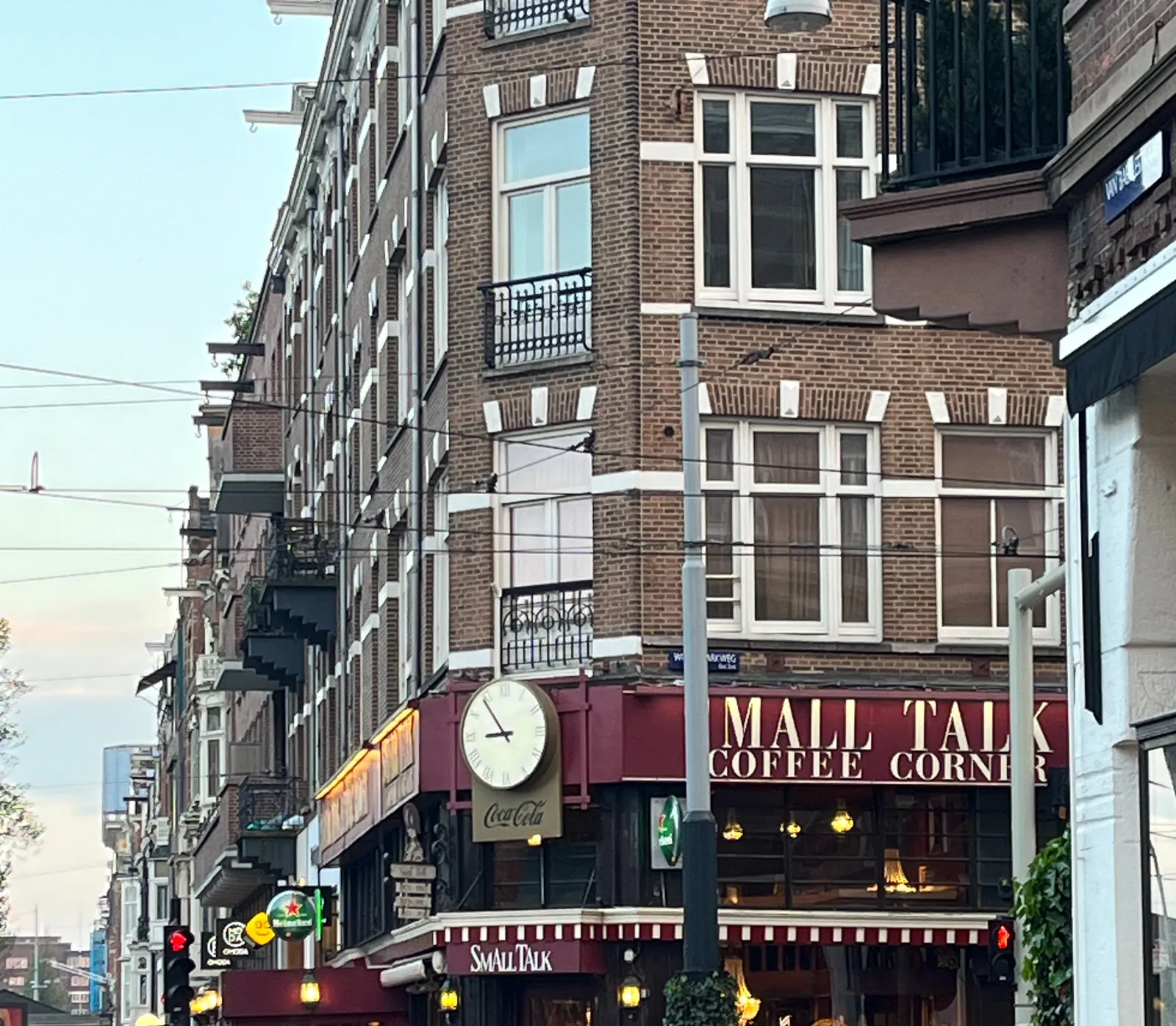 A cafe on a corner. It's called Small Talk. There’s a large clock above the door, which points at 6 minutes to 9.