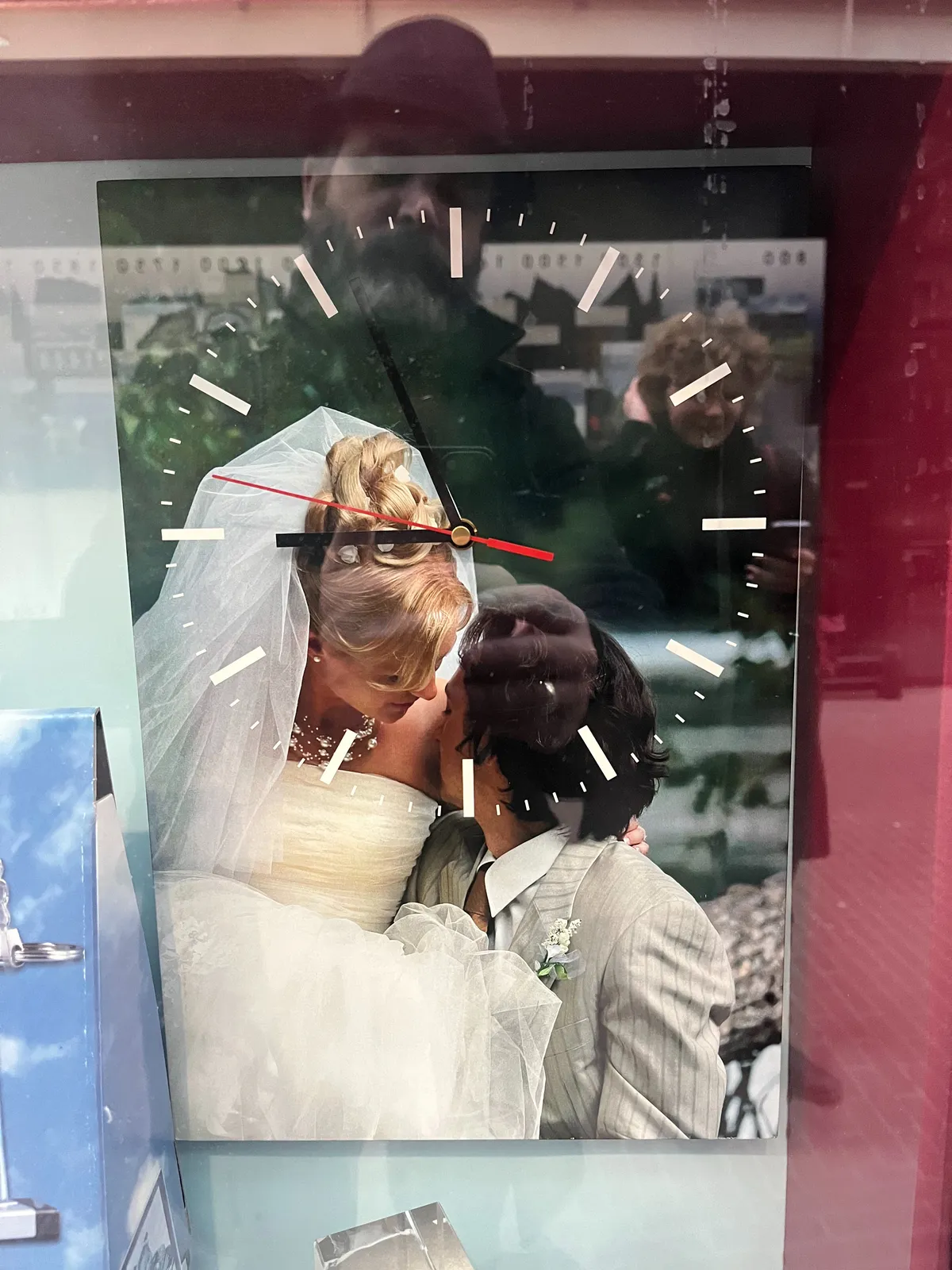 This picture of a couple who are getting married is also a clock. It points at 4 minutes to 9. It’s displayed behind glass, and the photographer (and his daughter) can be seen in the reflection.