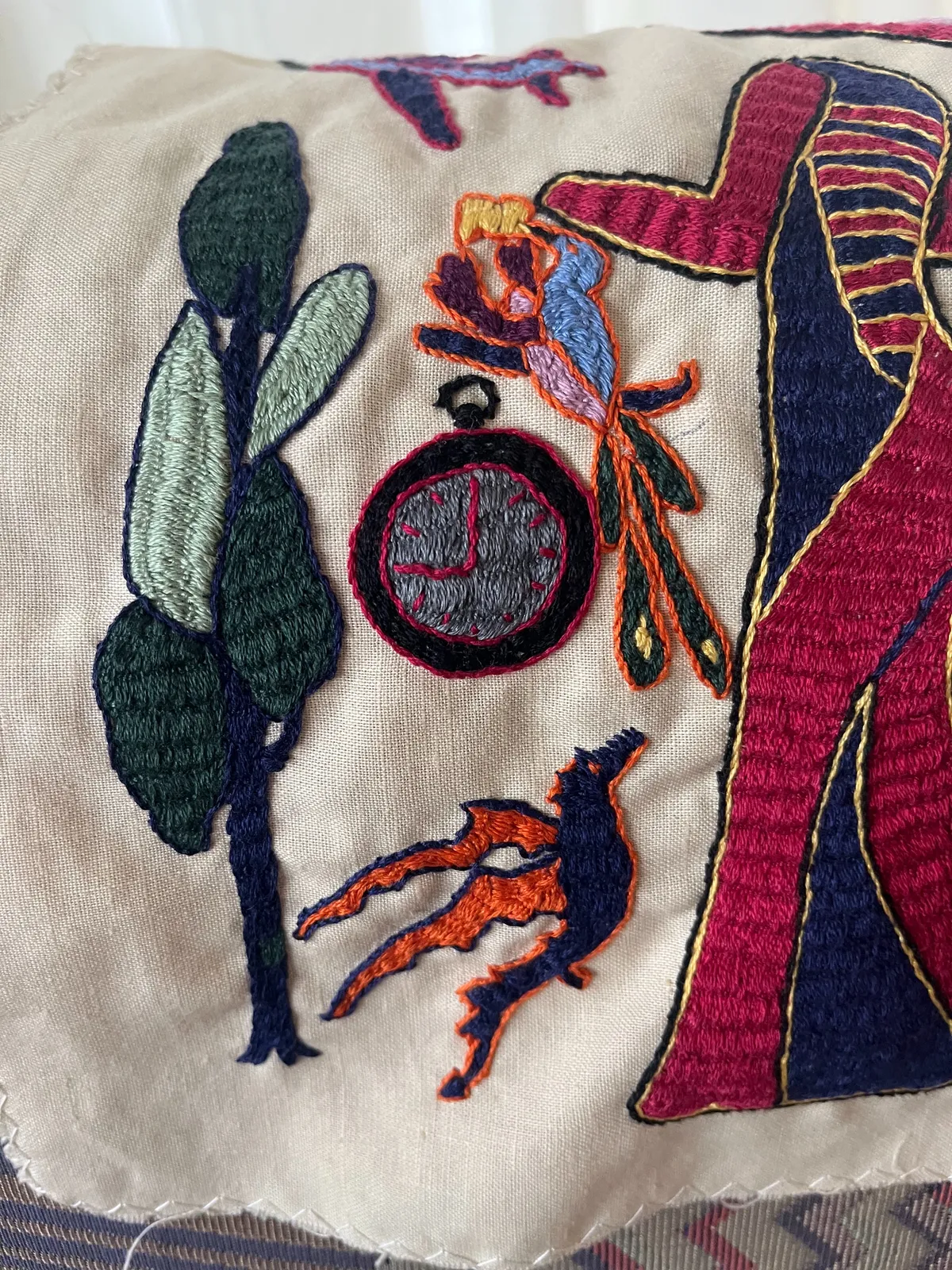 A detail of an embroidery. There’s an embroidered clock on it which points at nine o’clock.