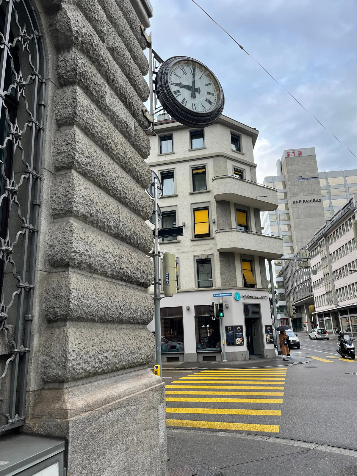 A clock attached to a heavy old building points at 1 past 9.