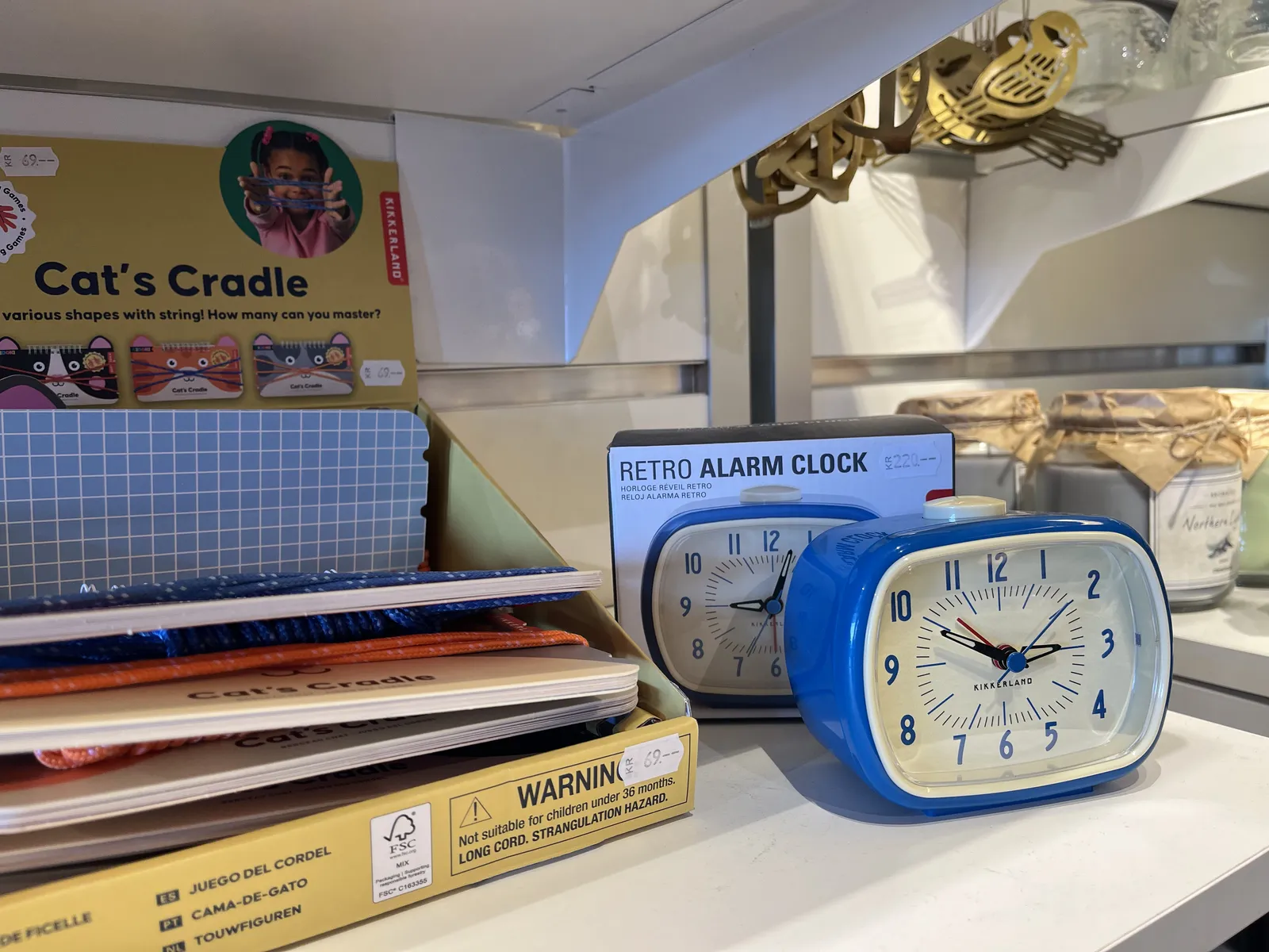 A shelf with some kids stuff for sale. Also for sale is a blue plastic clock, which stands in front of its box, with a picture of the same clock on it. Apparently this clock is called Retro Alarm clock. The real clock points at eleven minutes to three, the clock on the box points at three minutes past nine.