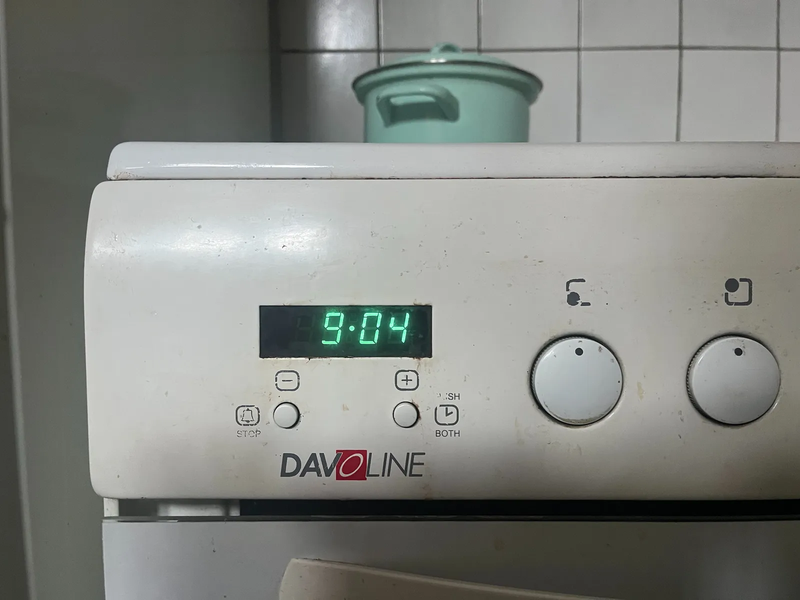 A turquise pan is standing on a stove. The digital clock on this stove displays the time as 09.04