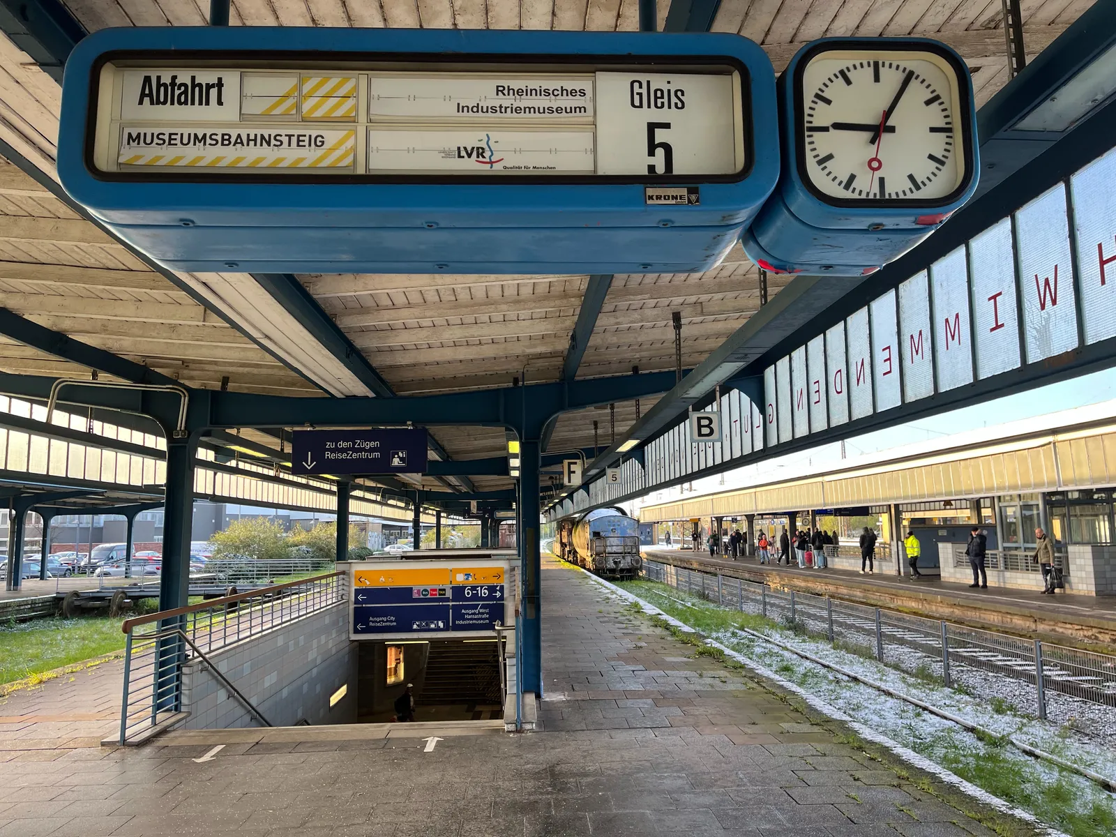 A mechanical display in a deserted train platform. The display says, in German, that this is the Museum Platform from the Reinisches Industriemuseum. The clock next to the display points at 5 past 9.