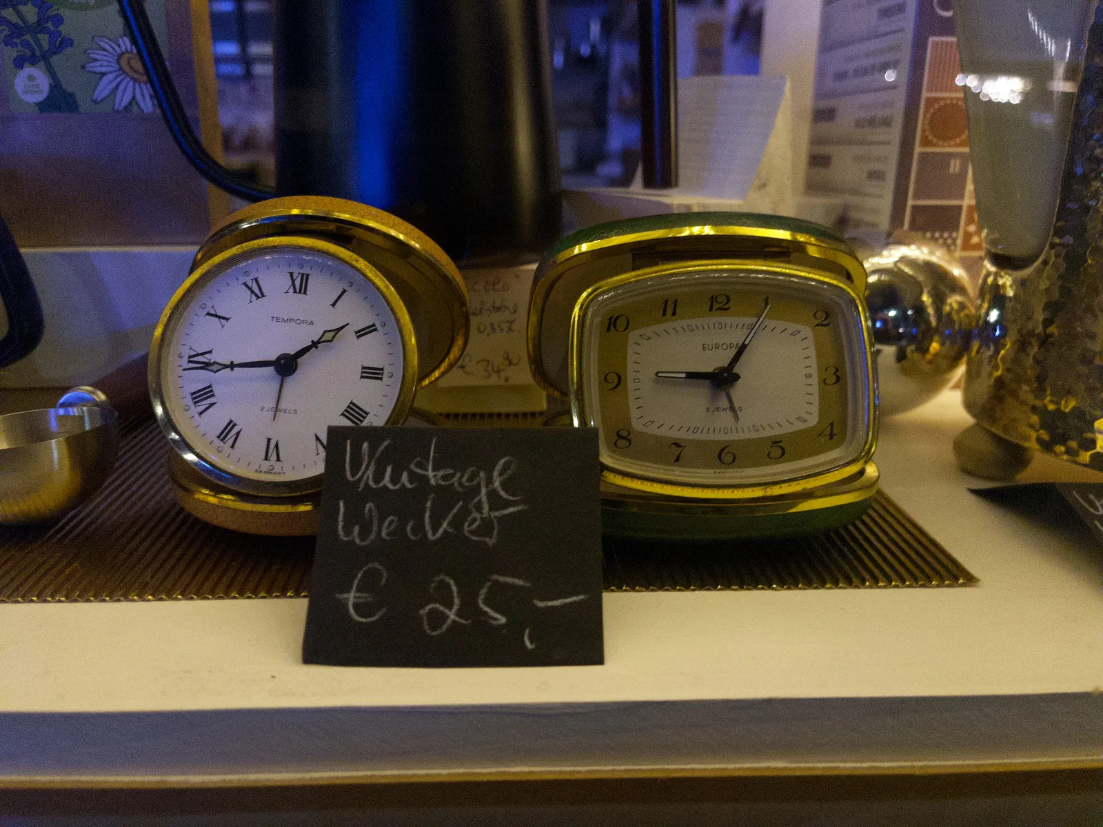 Two vintage travel clocks in a shop window. One of them points at 17 minutes to two, the other at six minutes past nine.