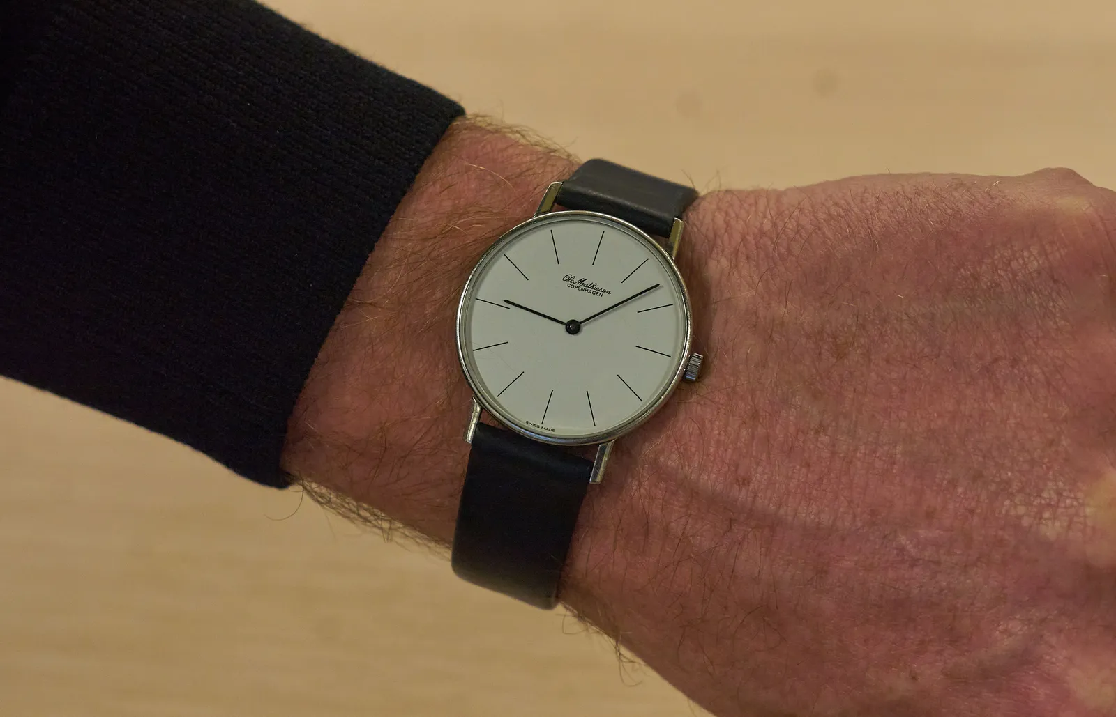 A minimalist wrist watch points at approximately eight past nine.