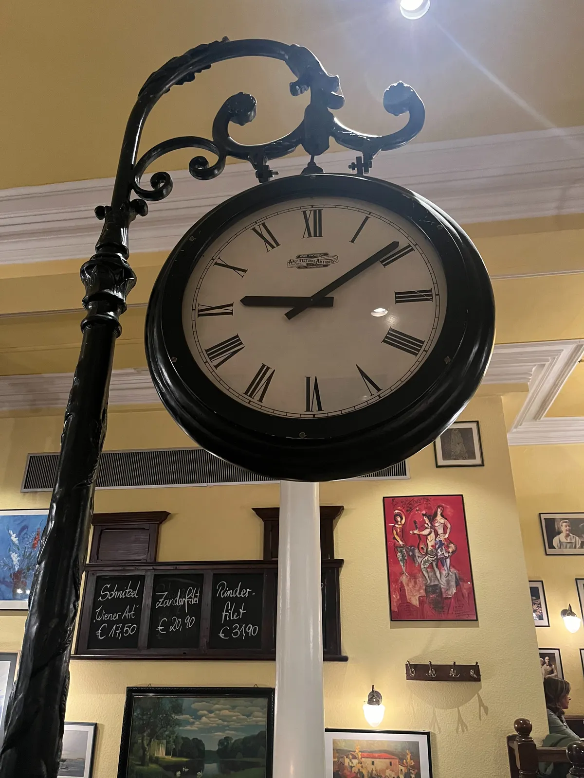 A large clock hanging from a pole inside a restaurant. It points at 9 minutes past 9.