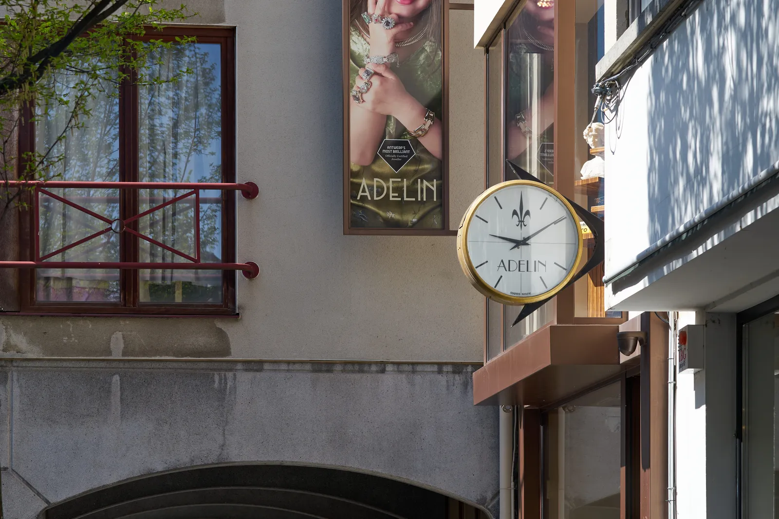 A clock attached to a shop that’s called Adelin. The clock points at 9 past 9.