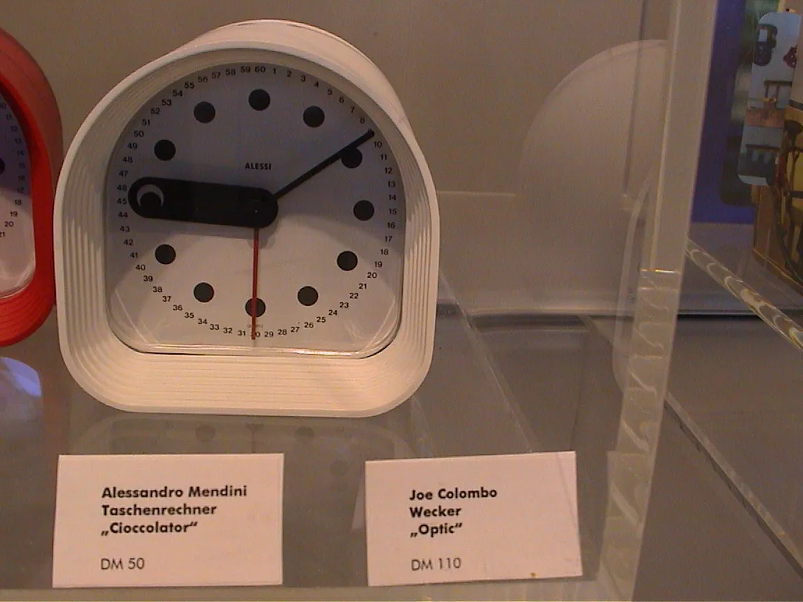 On a sign in a german store it says this is a Joe Colombo Optic Wecker. The time on this Wecker is nine past nine.
