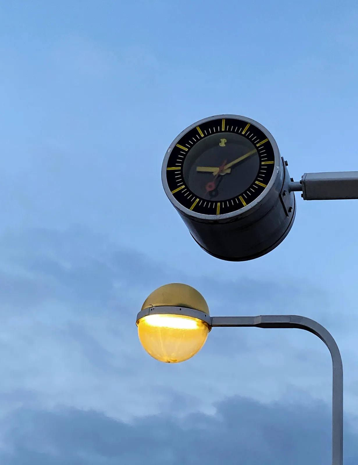 A round street lamp next to a round station clock, the ones you find in the Amsterdam metro. The clock points at 10 past 9.