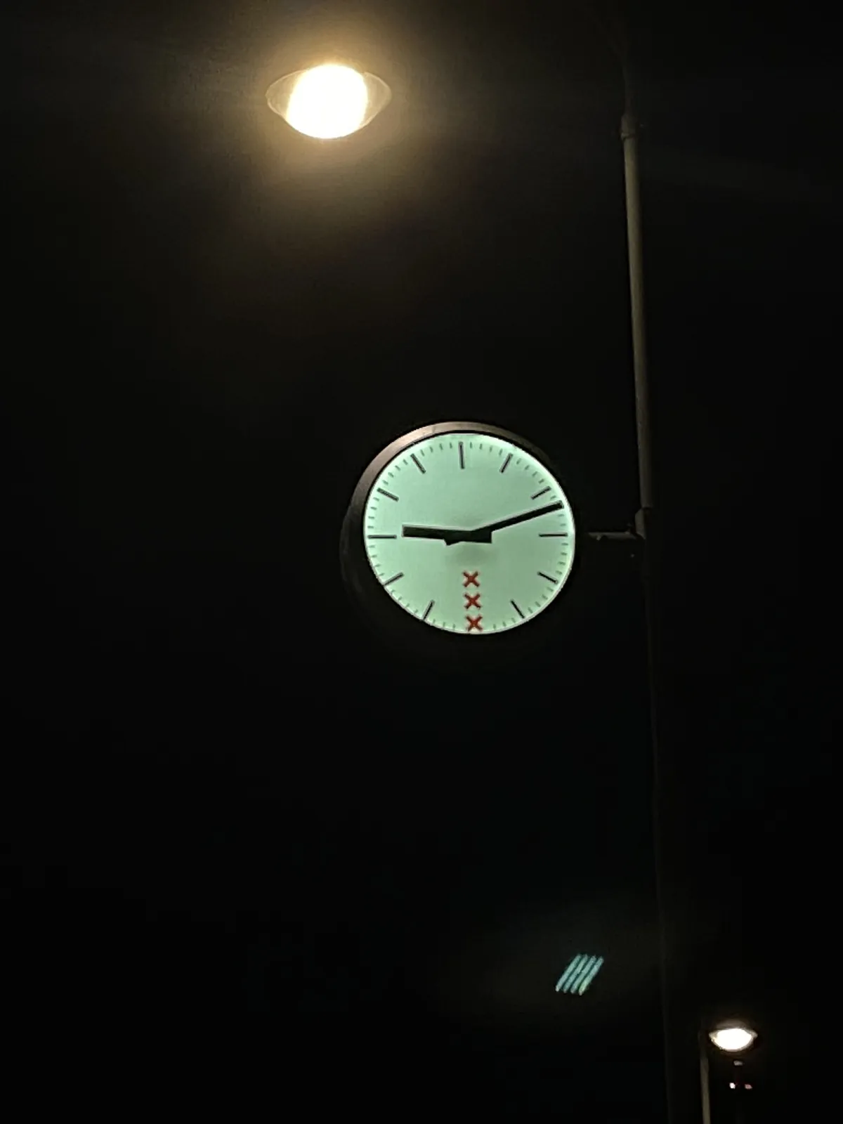 A clock in Amsterdam. It is dark around it. It points at 12 past 9.