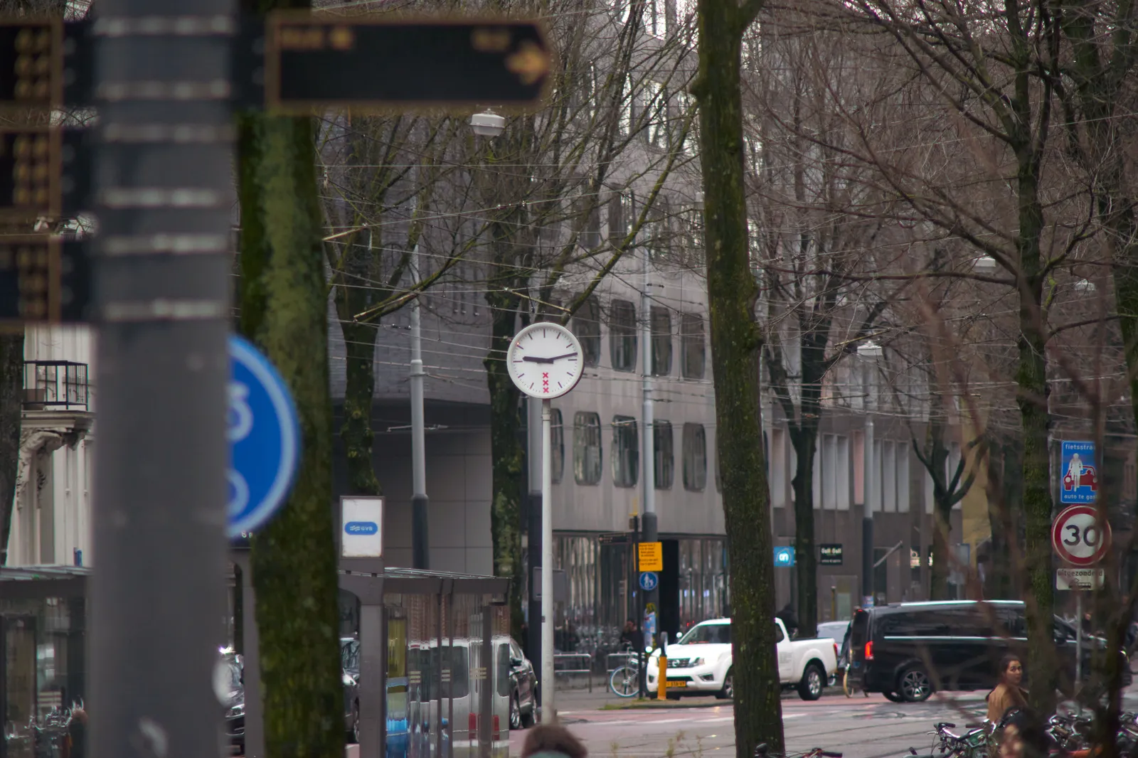 Lots of trees, buildings, cars, street signs and in this middle there’s this clock which points at 13 past nine.
