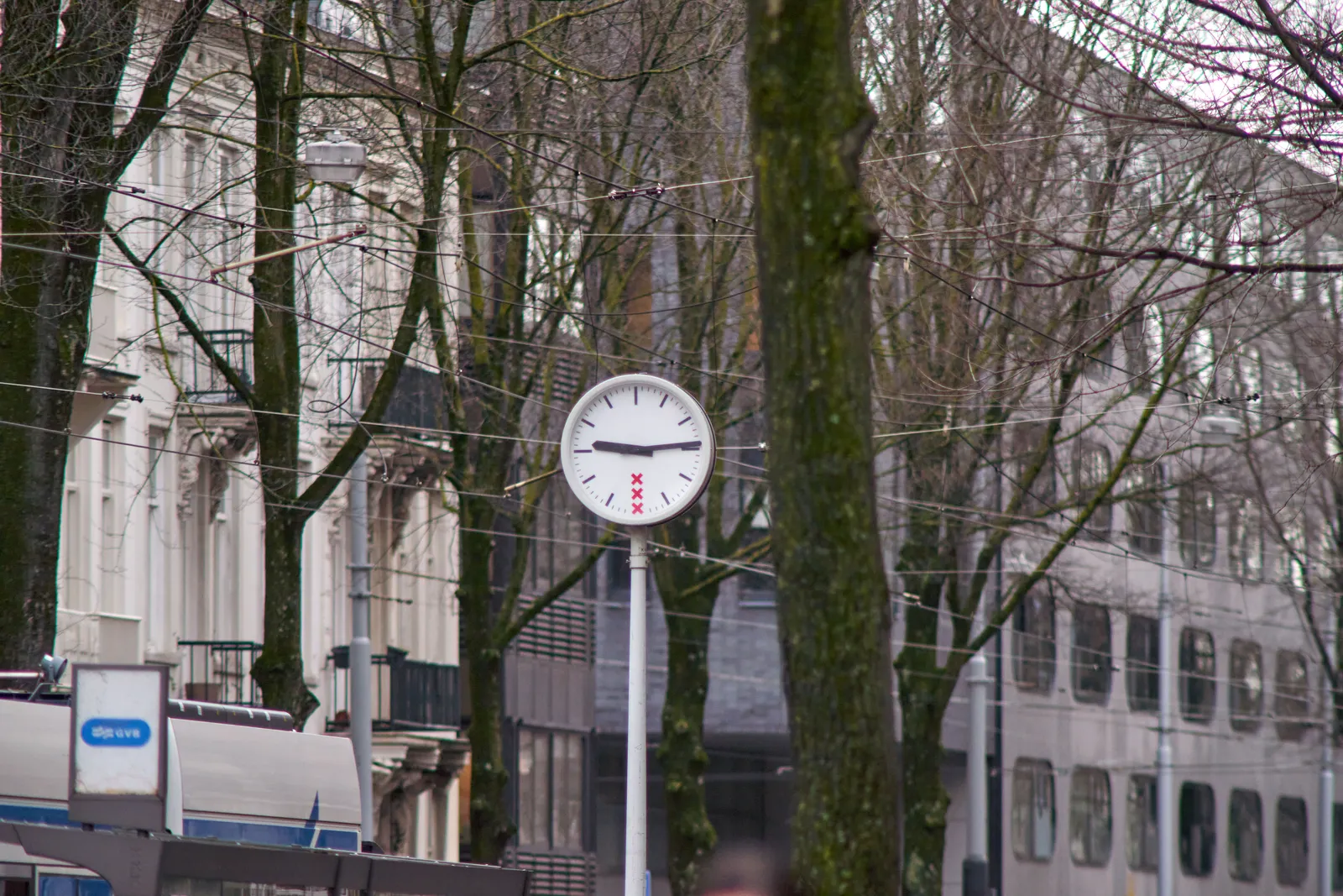 Some trees, some buildings, a part of a tram stop, and in the middle there’s a clock. It points at 14 past nine.
