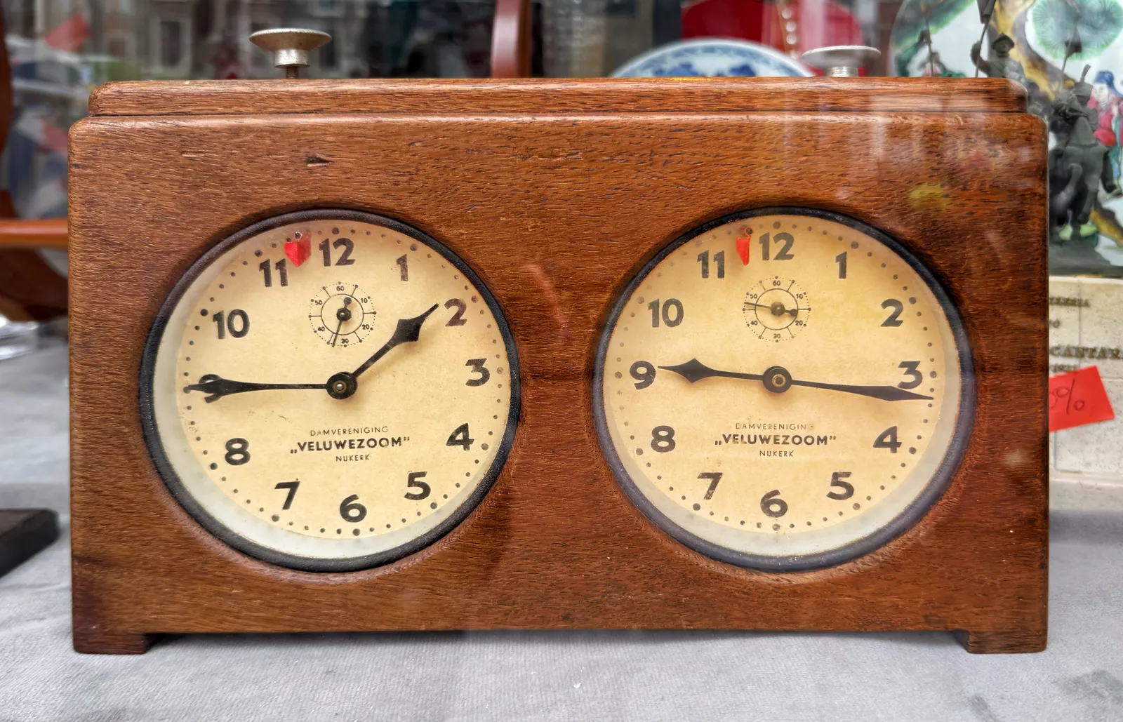 This looks like a chess clock, but if you look closely at the words on the two clocks you’ll see that this is a draughts clock. It’s made from wood. On both faces it says Damvereniging Veluwezoom Nijkerk, a Dutch draughts club. The clock on the left points at a quarter to two, the one on the right at 16 minutes past nine.