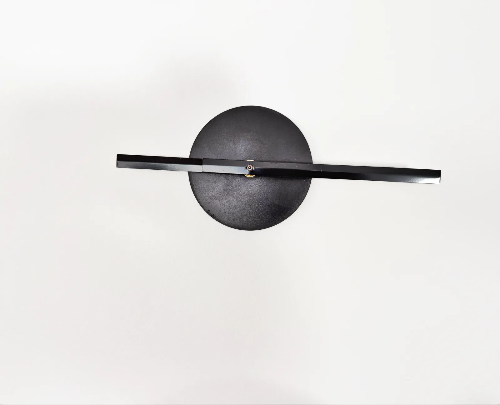 A very minimalist clock. Just two black hands on a white wall. They point in exactly the opposite direction, at 16 minutes past nine.