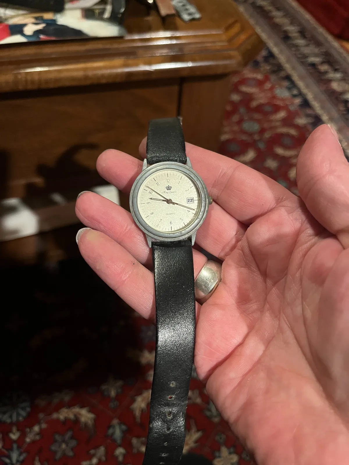 Someone is holding an old watch in their hand. In the background, blurry, an old Persian rug. The watch points at 18 minutes past nine.
