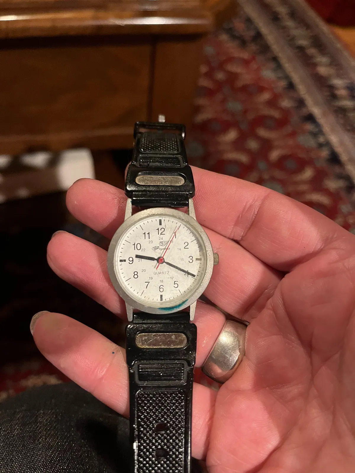 Someone is holding an old watch in their hand. In the background, blurry, an old Persian rug. The watch points at 19 minutes past nine.