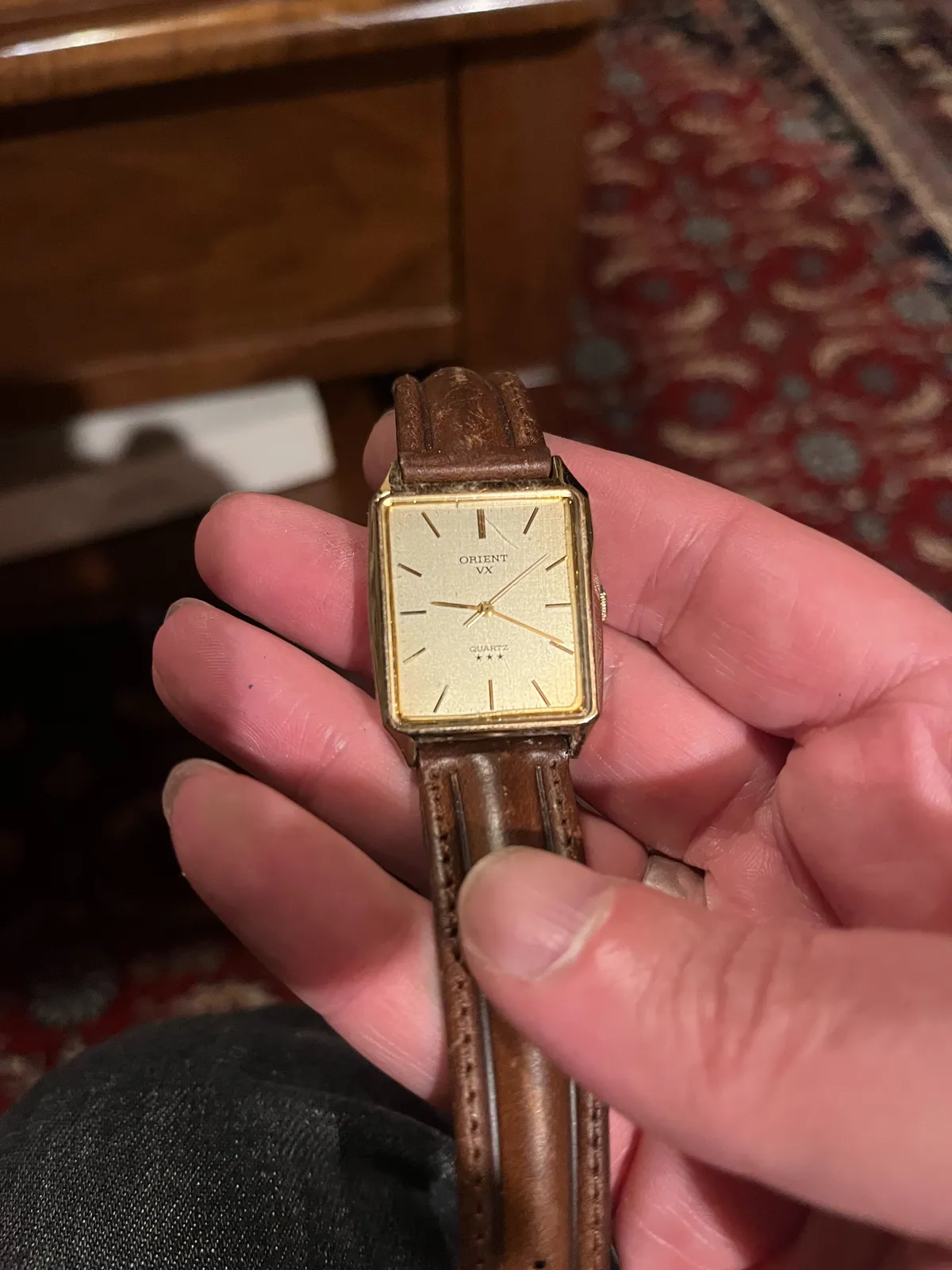 Someone is holding an old watch in their hand. In the background, blurry, an old Persian rug. The watch points at 19 minutes past nine.