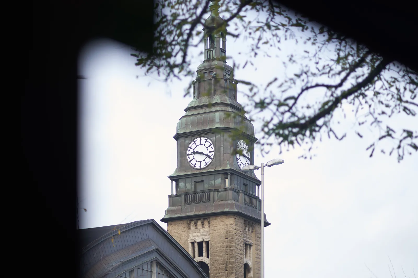 Looking out the window of a bus at a large tower with clocks on it. On one clock you can see clearly that it’s 19 minutes past 9.