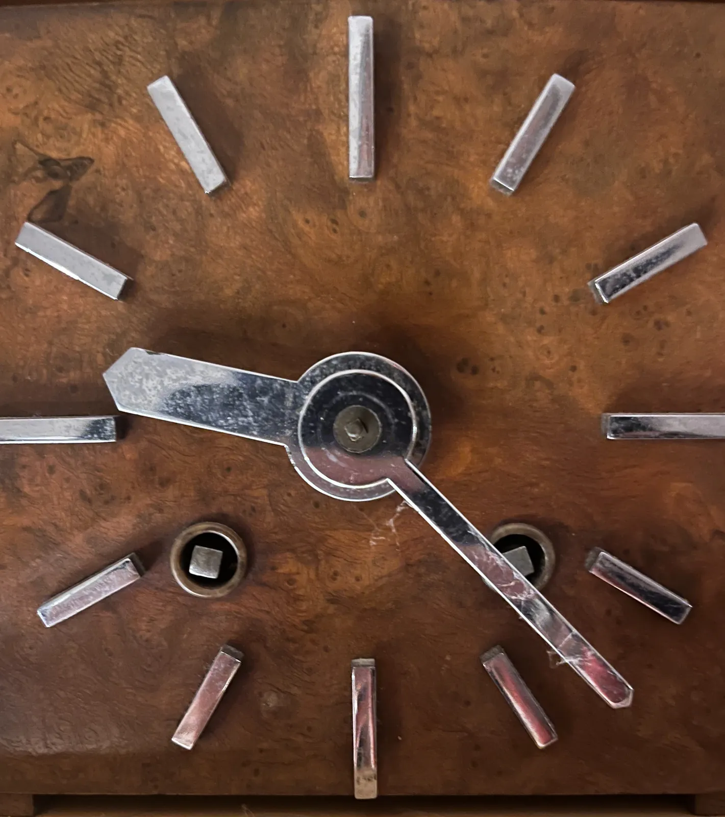 A closeup of the face of an old, wooden clock. It seems to be made from walnut. It points at 23 minutes past 9.