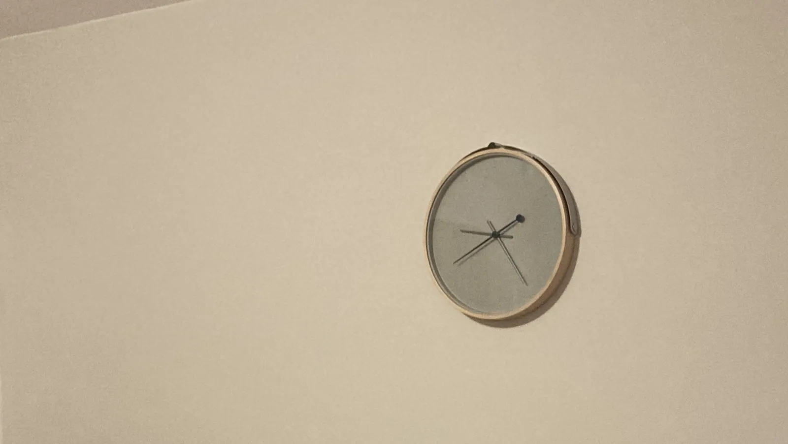 A minimalist clock on a white wall. It points at roughly 24 minutes past 9.