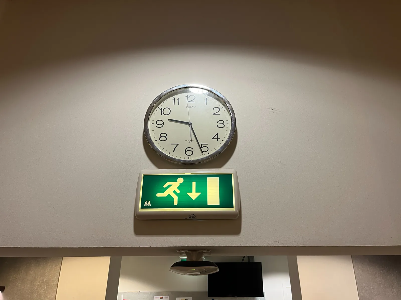 Above a sign that points towards the exit there’s a clock that points at 26 minutes past 9.