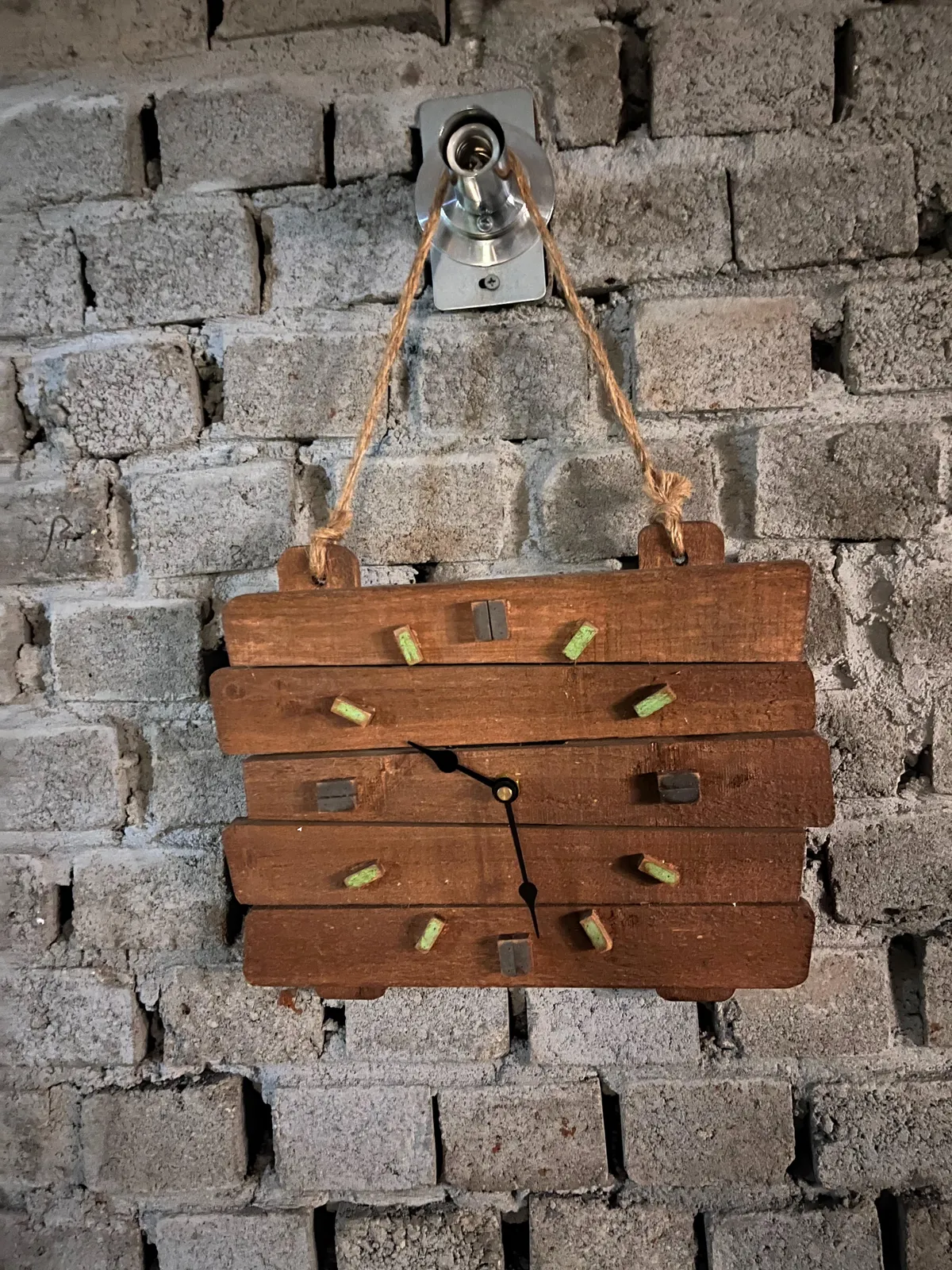 A wooden clock, a bit shoddy, on a brick wall, also a bit shoddy. The clock points at approximately 28 minutes past 9.