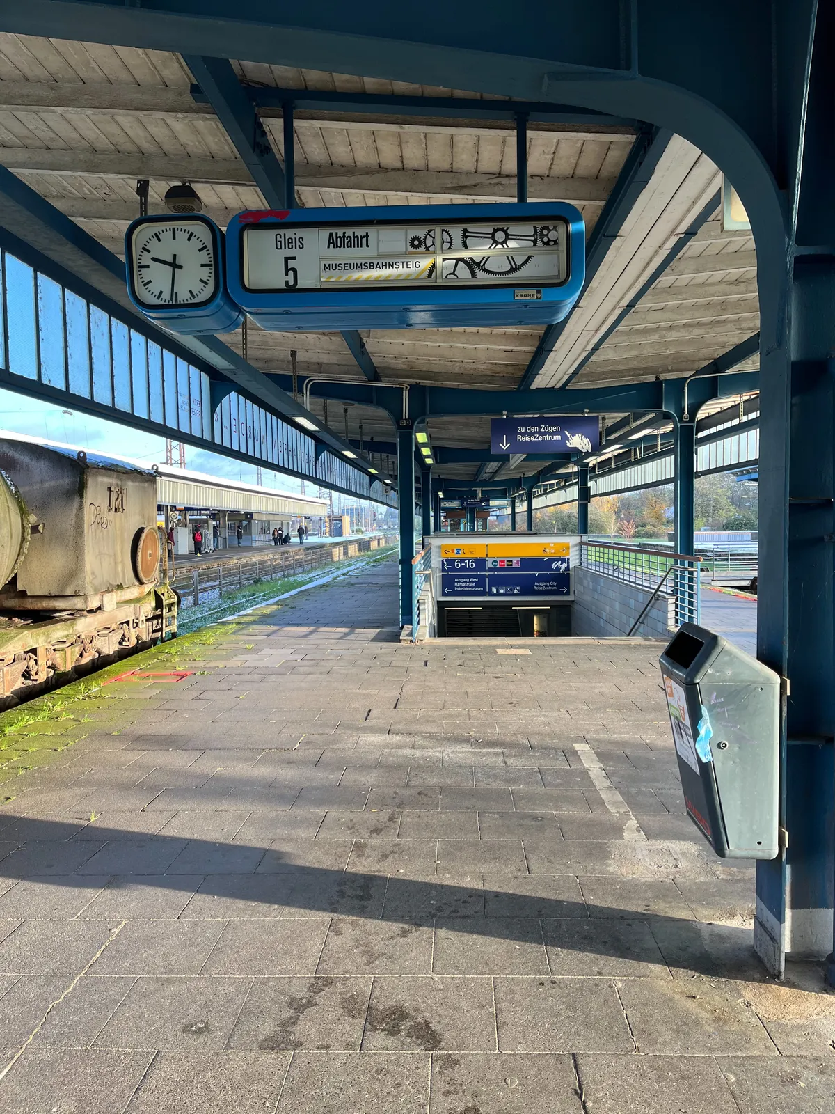 A mechanical display in a deserted train platform. The display says, in German, that this is a Museum Platform. The clock next to the display points at 5 past 9.