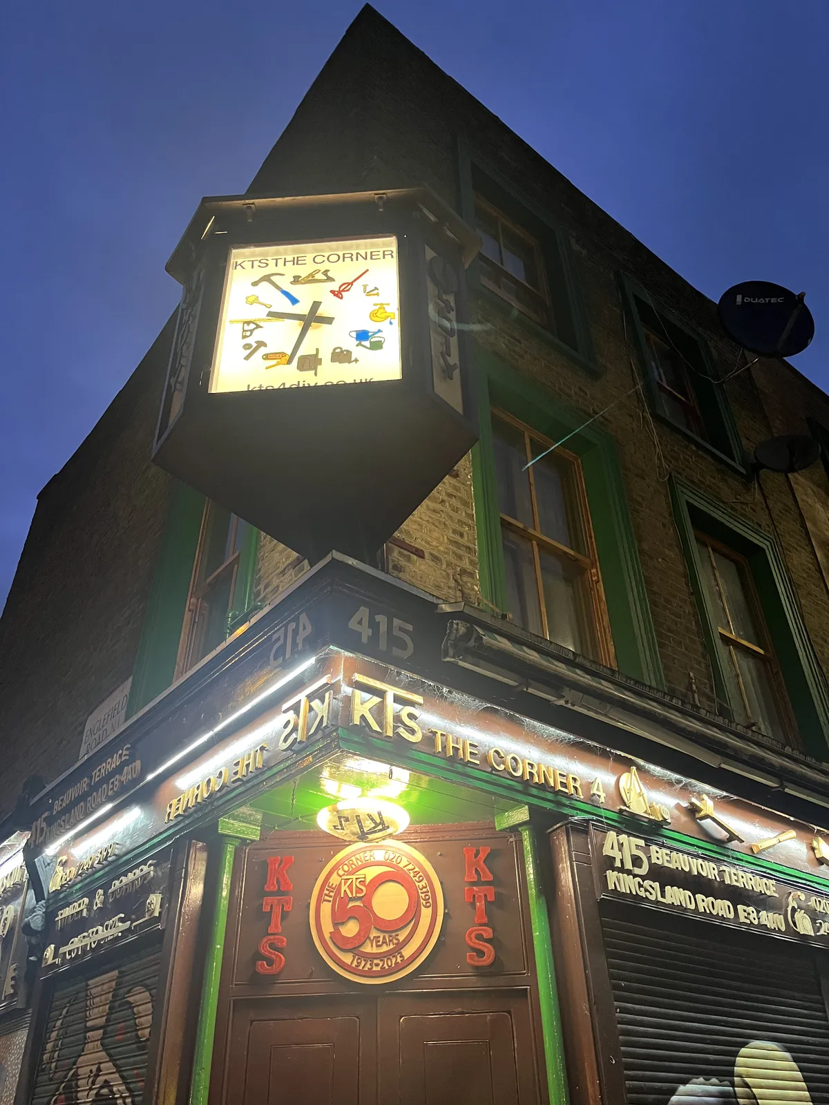 A lit clock attached to the corner of the KTS The Corner shop. It points at 32 minutes past nine.