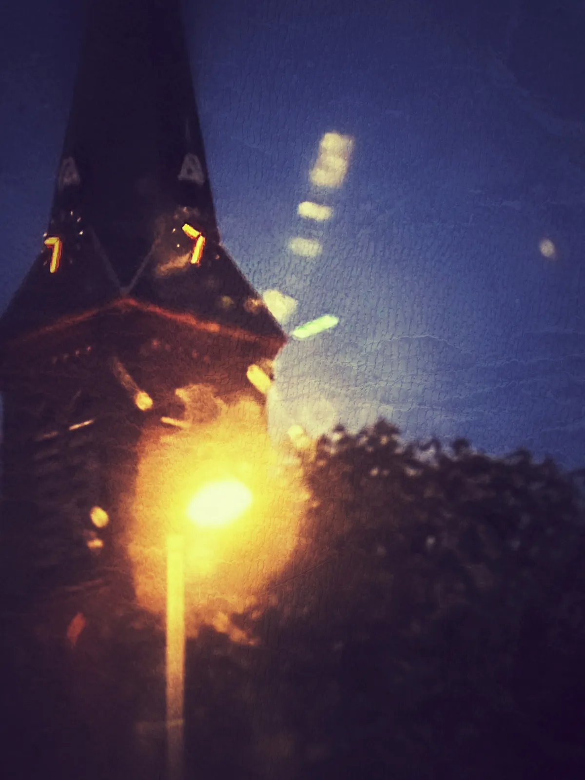 A rather blurry picture of a street light in the front, and a church tower in the back. There are two lit clocks on this tower that both point at 32 minutes past 9.