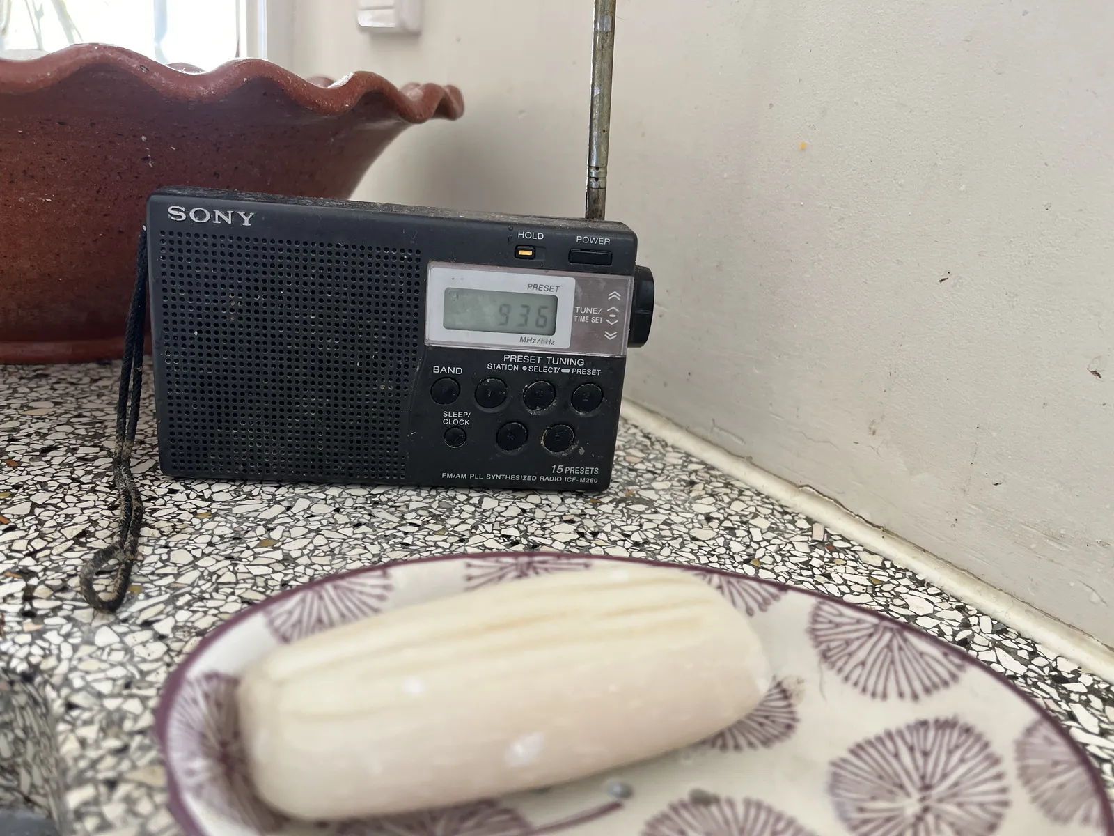 A plate with a soap bar, with behind it an old Sony radio with a small digital display that shows the time as 09:36