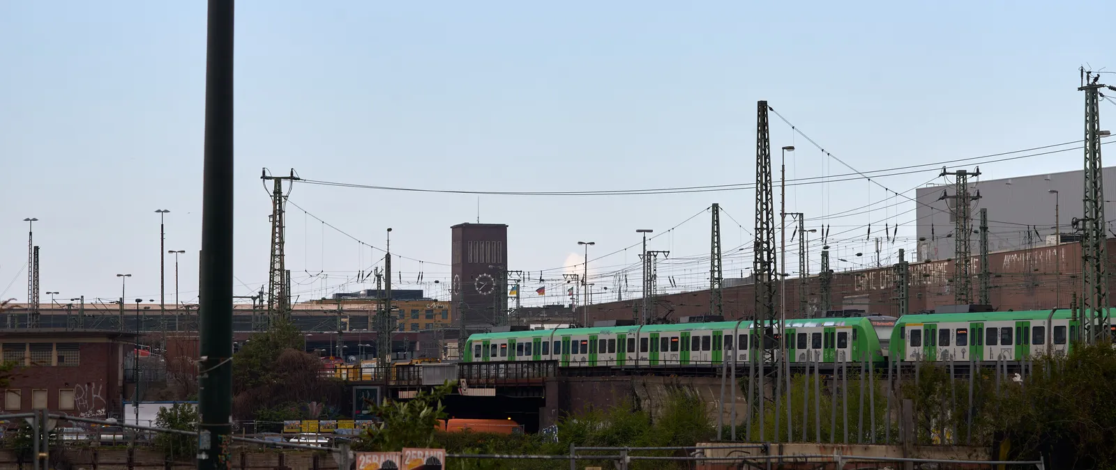 A train is running in a city scape. In the distance the Düsseldorf train station tower with its clock can be seen. It points at 37 past 9.